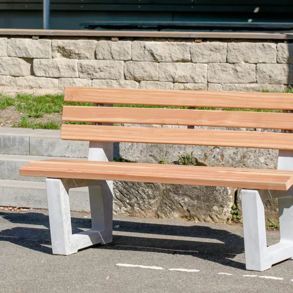 Ergonomische Sitzbank mit Lärchenholzlatten und Füßen aus Beton steht an einem öffentlichen Weg