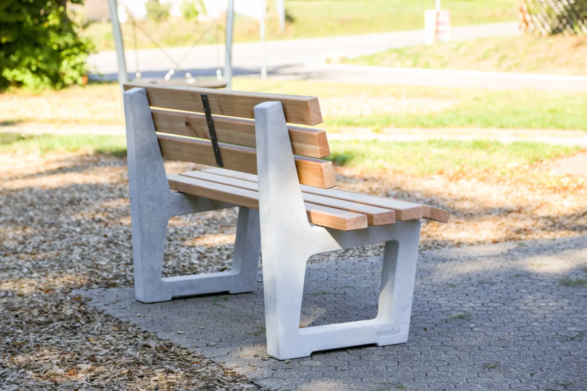 Ergonomische Sitzbank mit Lärchenholzlatten und Füßen aus Beton steht an einem öffentlichen Weg