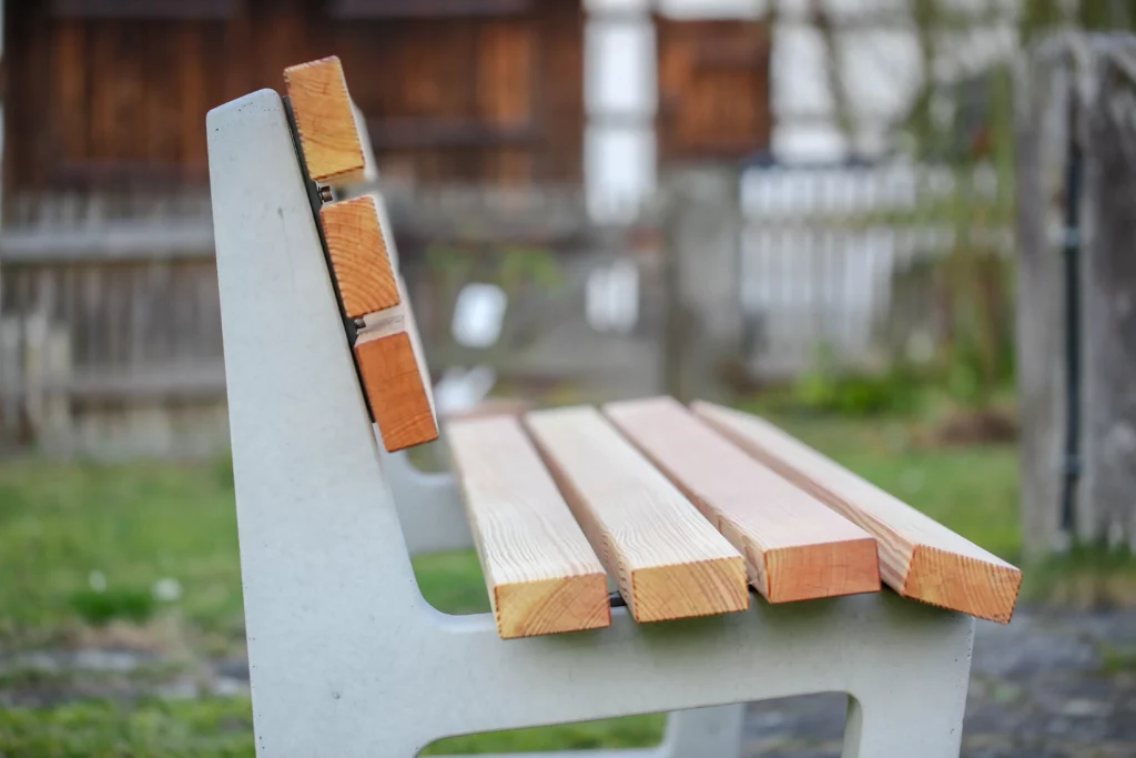 Ergonomische Sitzbank mit Lärchenholzlatten und Füßen aus Beton steht an einem öffentlichen Weg