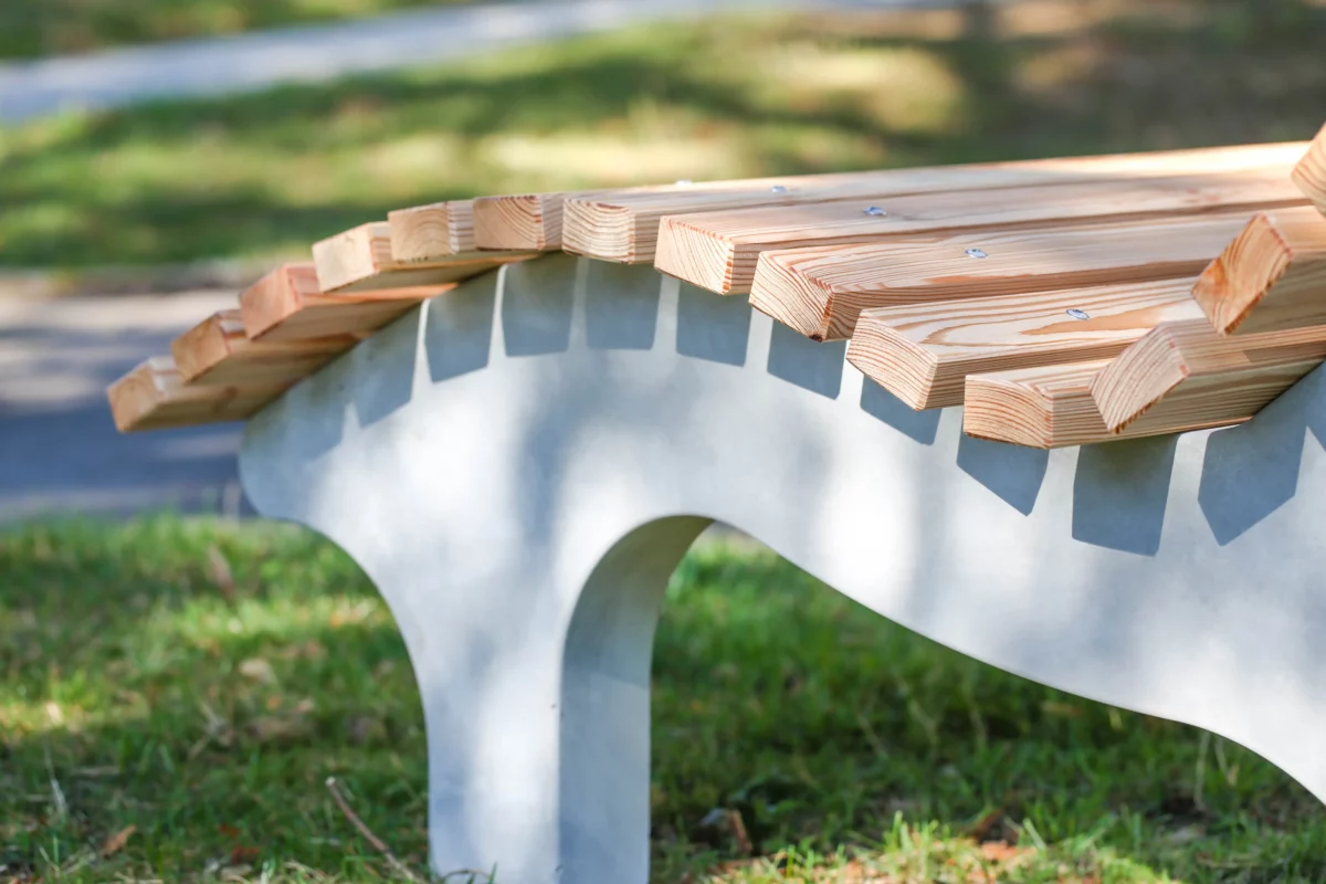 Wellenliege aus Beton und Lärchenholz steht in einem begrünten Außenbereich