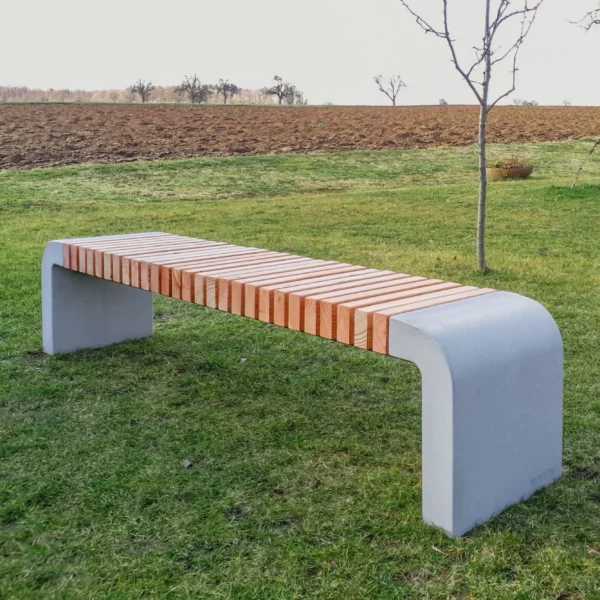 Moderne Sitzbank mit abgerundeten Füßen aus Beton und längs verlaufenden Holzlatten steht in einer öffentlichen Grünanlage.