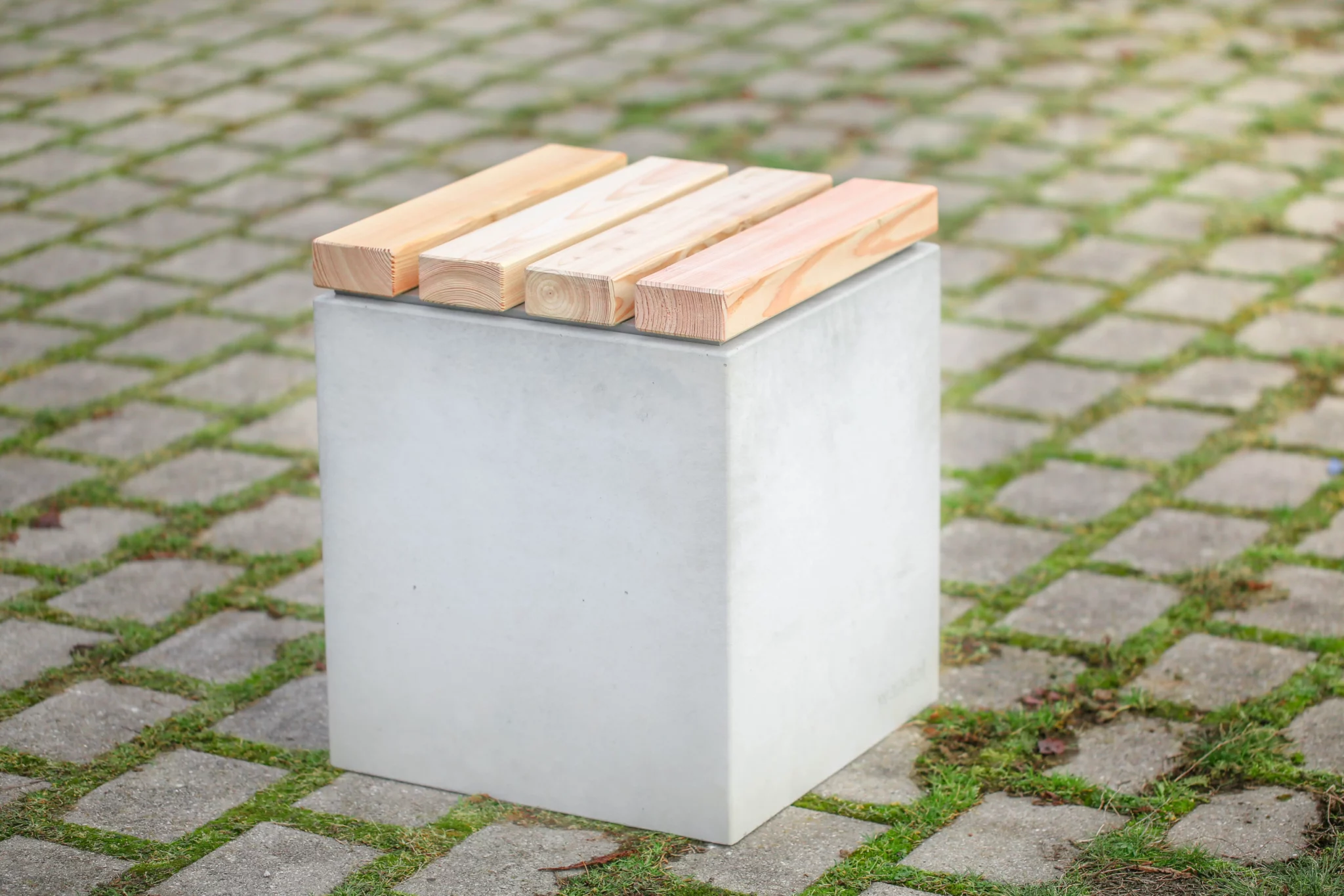 Hocker aus Beton mit Sitzauflage aus Lärchenholz steht auf öffentlicher Grünanlage