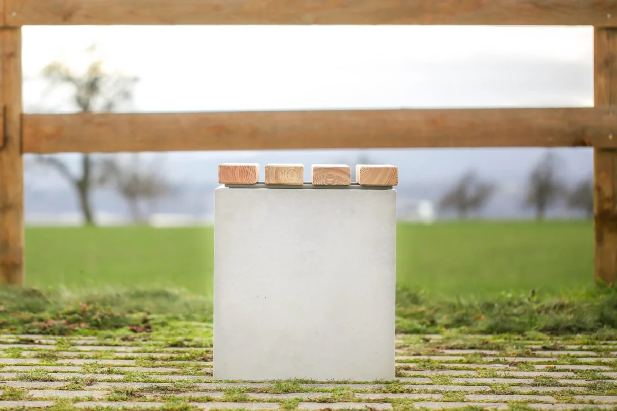 Hocker aus Beton mit Sitzauflage aus Lärchenholz steht auf öffentlicher Grünanlage