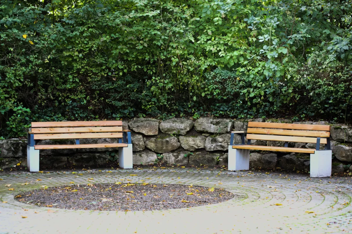 Armlehne feuerverzinkt mit Lärchenholzauflage zum optionalen Aufschrauben auf Outdoor-Sitzbank steht in einem öffentlichen Bereich