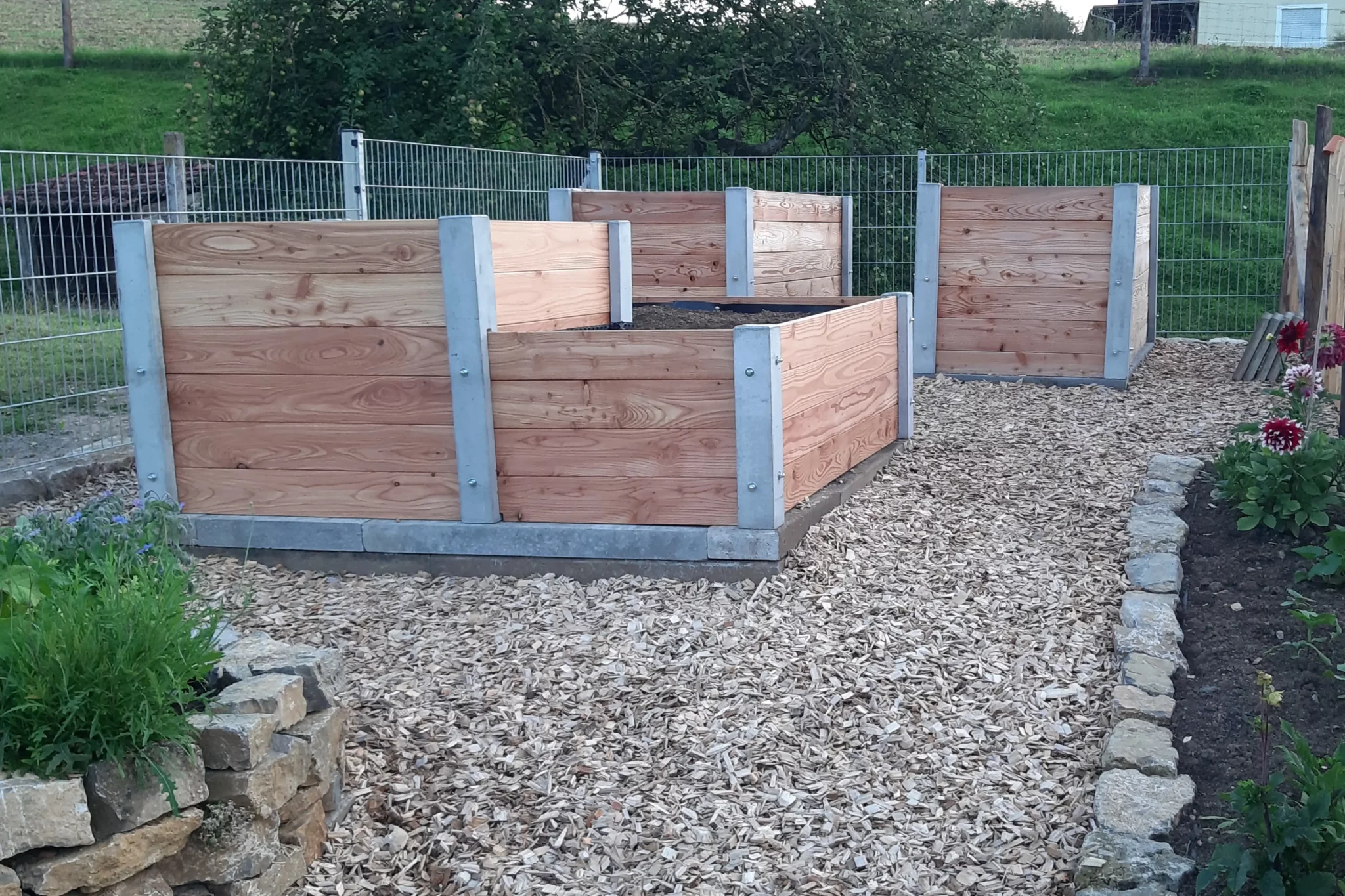Hochbeet über Ecke aus Lärchenholz und Beton steht in einem privaten Garten mit viel Grün