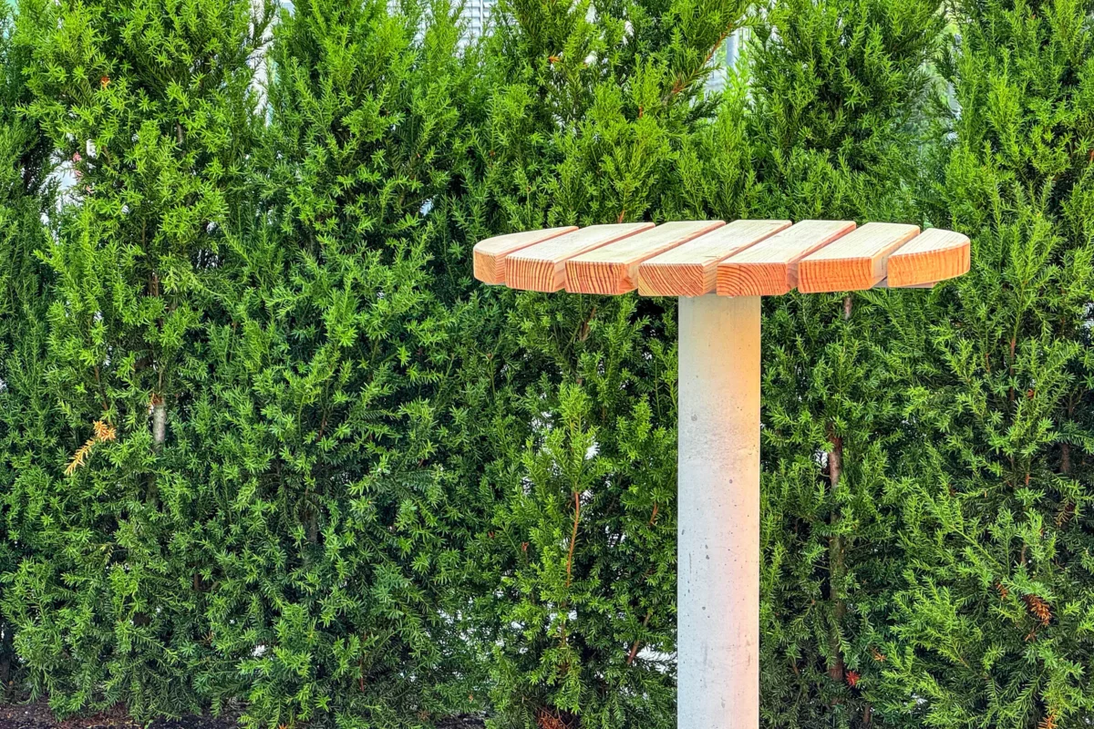 Stehtisch mit Betonfuß zum Einbetonieren und Auflage aus Lärchenholz steht in Mitarbeiterbereich eines Firmengeländes